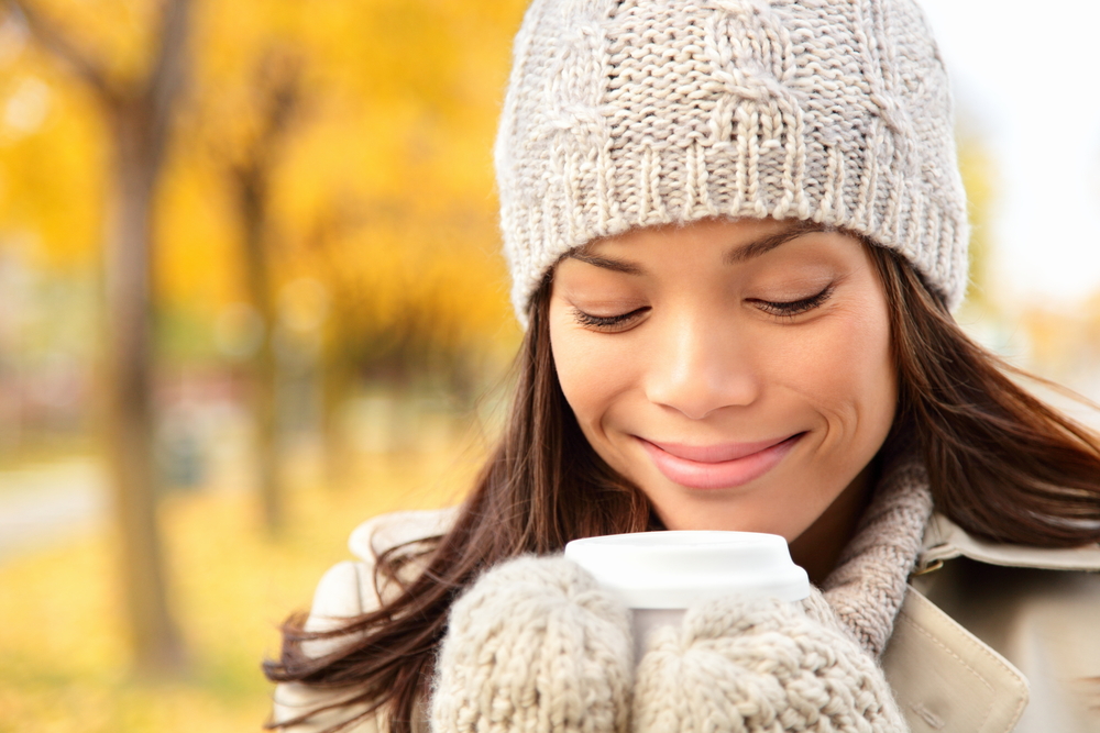 Woman with a hat and mittens enjoying coffee outside
