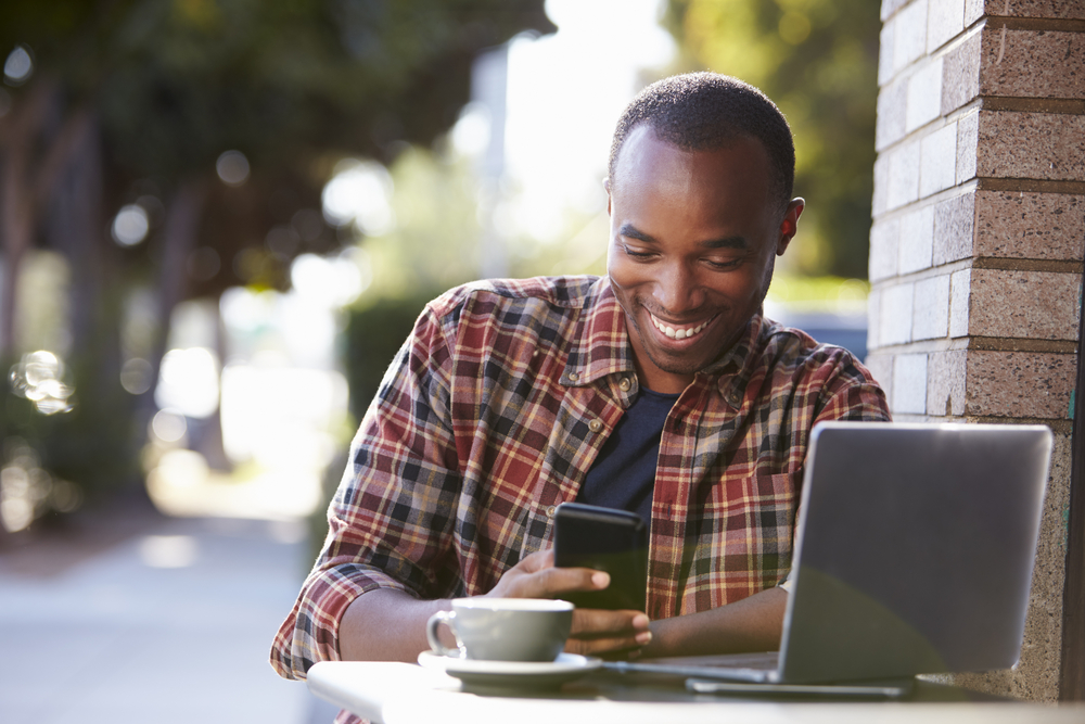 Un homme avec un ordinateur portable et une tablette qui regarde son téléphone