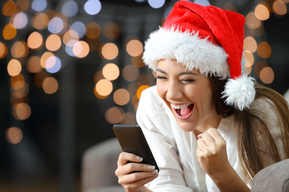 Excited woman with a Santa hat looking at her cell phone