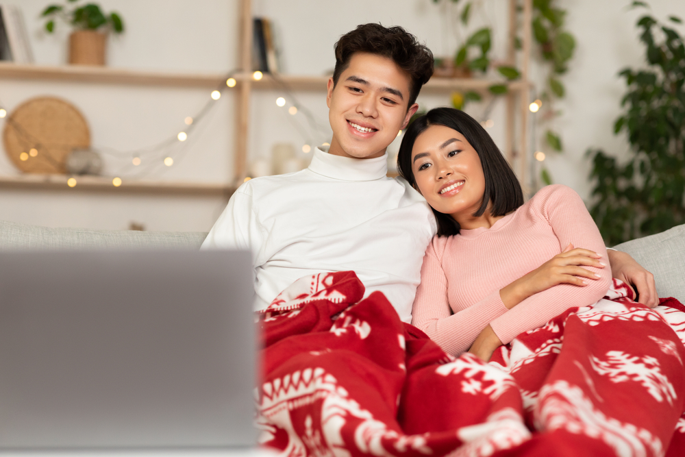 Young couple watching movies virtually with their friends on their laptop