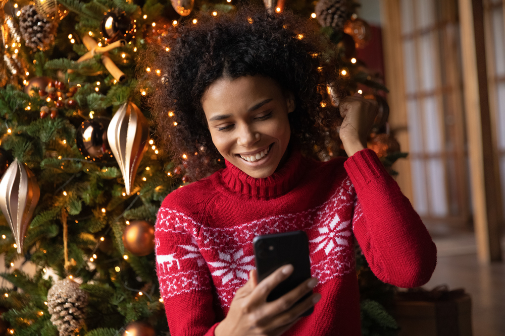 Woman in a holiday sweater playing online games with her friends on her cellphone