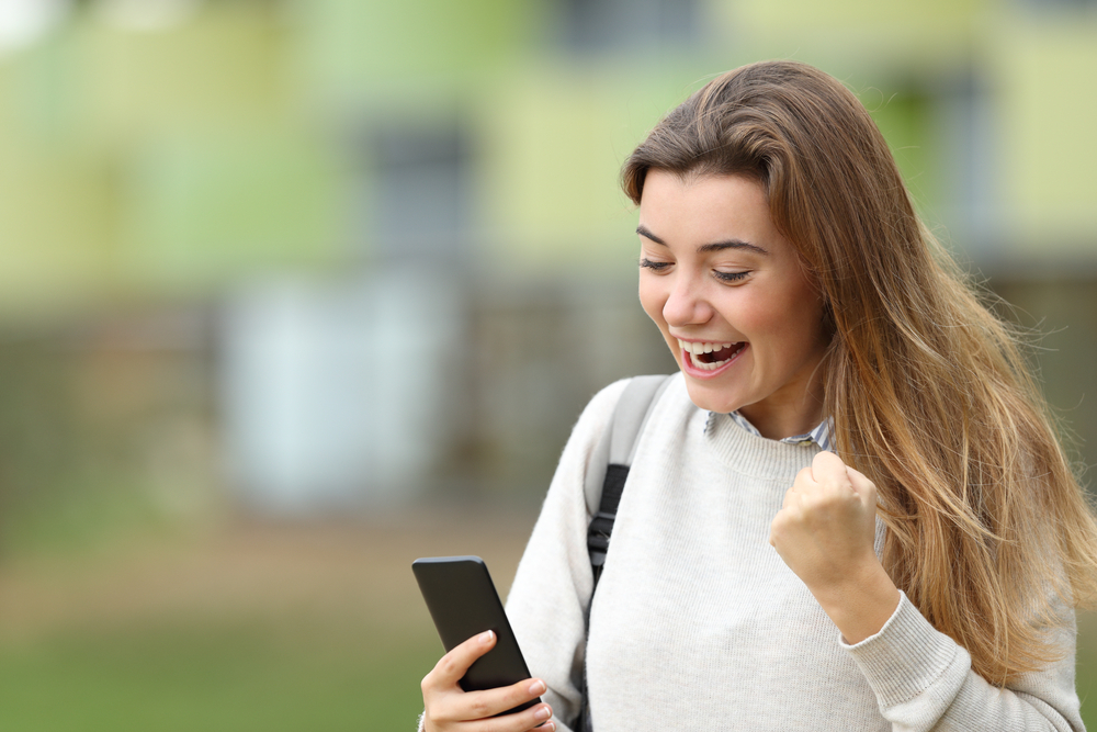 Young woman looking at her cellphone and celebrating