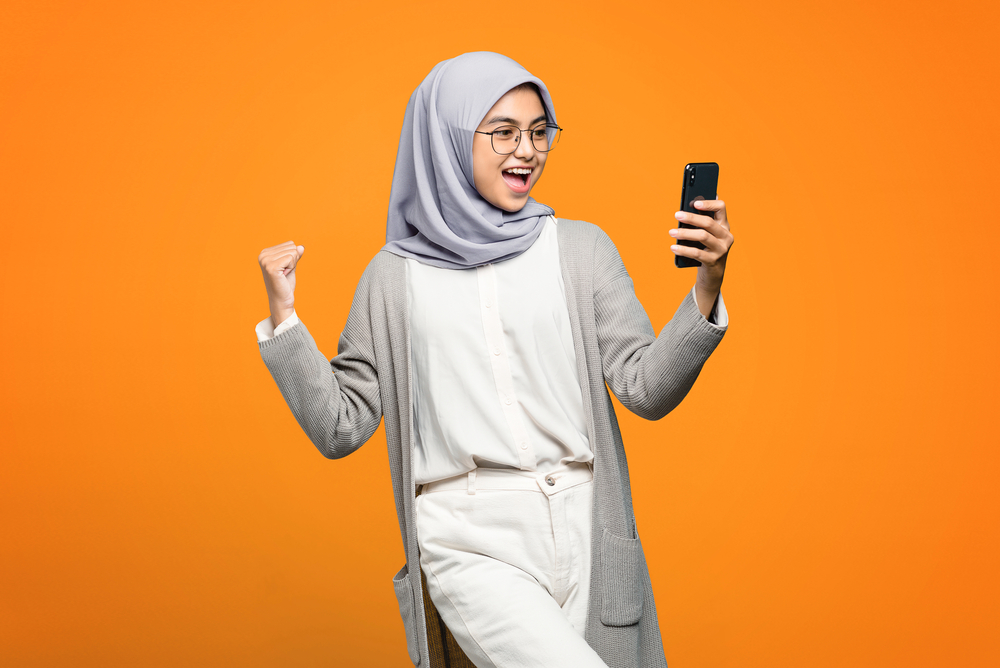 Une femme heureuse regarde son cellulaire pour découvrir les nouveaux concours LEO.