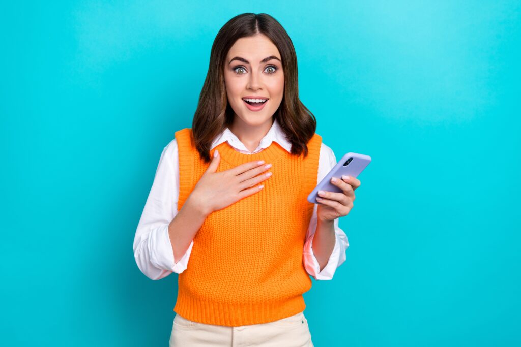Une femme heureuse portant un vêtement orange est surprise par son téléphone