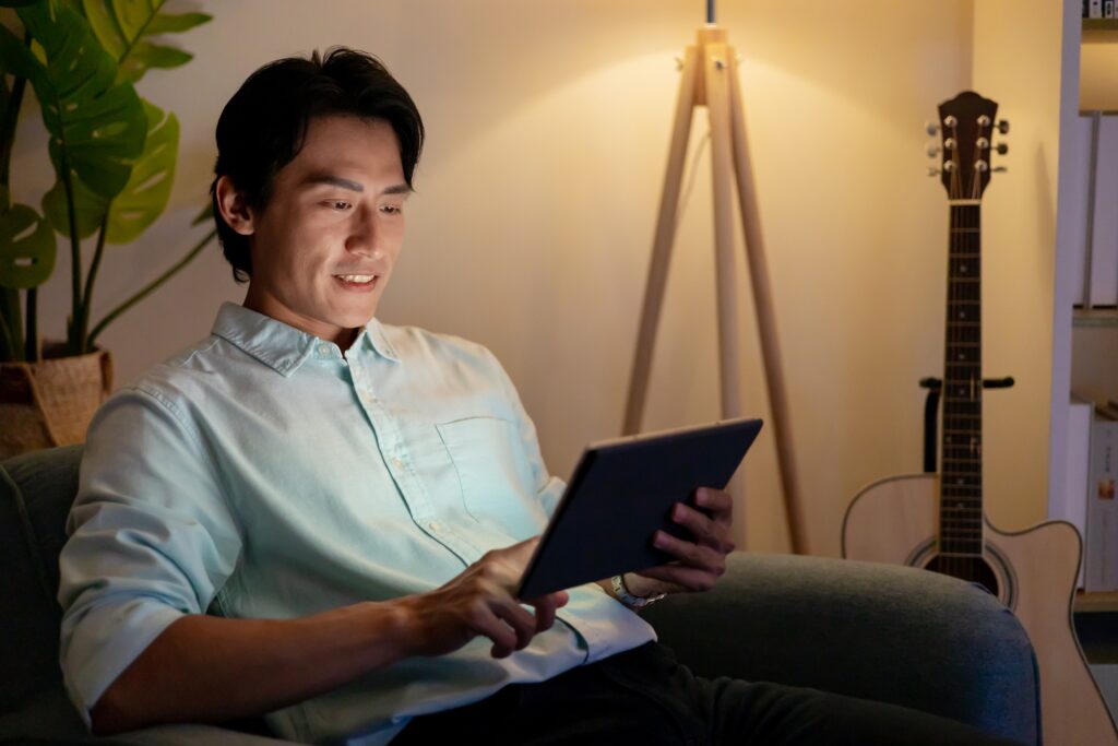 Homme lisant le blog LEO sur une tablette à la maison dans une ambiance chaleureuse du soir, avec une guitare et un éclairage doux en arrière-plan.