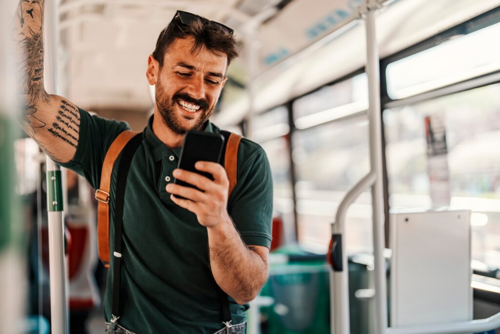 Smiling young man standing on public transport, using the LEO platform on his smartphone for an effortless digital experience on the go.