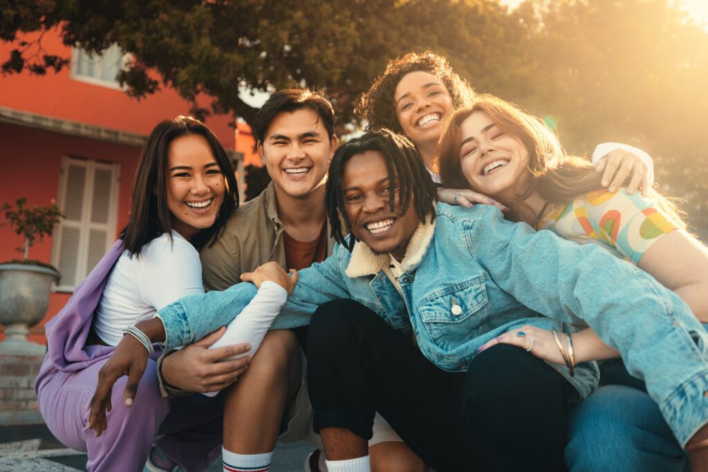 According to Happy Cities study, young people are embracing life, shown by a diverse group of smiling friends enjoying time together outdoors in the sun.