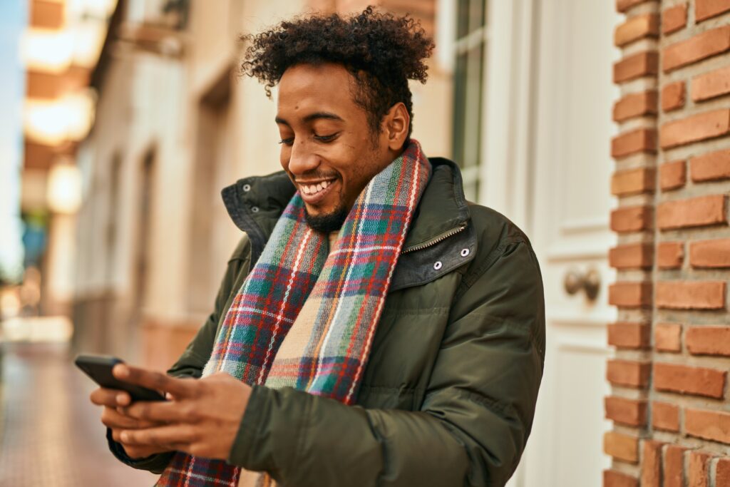 Smiling man outdoors in winter clothes and scarf using his smartphone, answering a LEO survey while walking down the street.