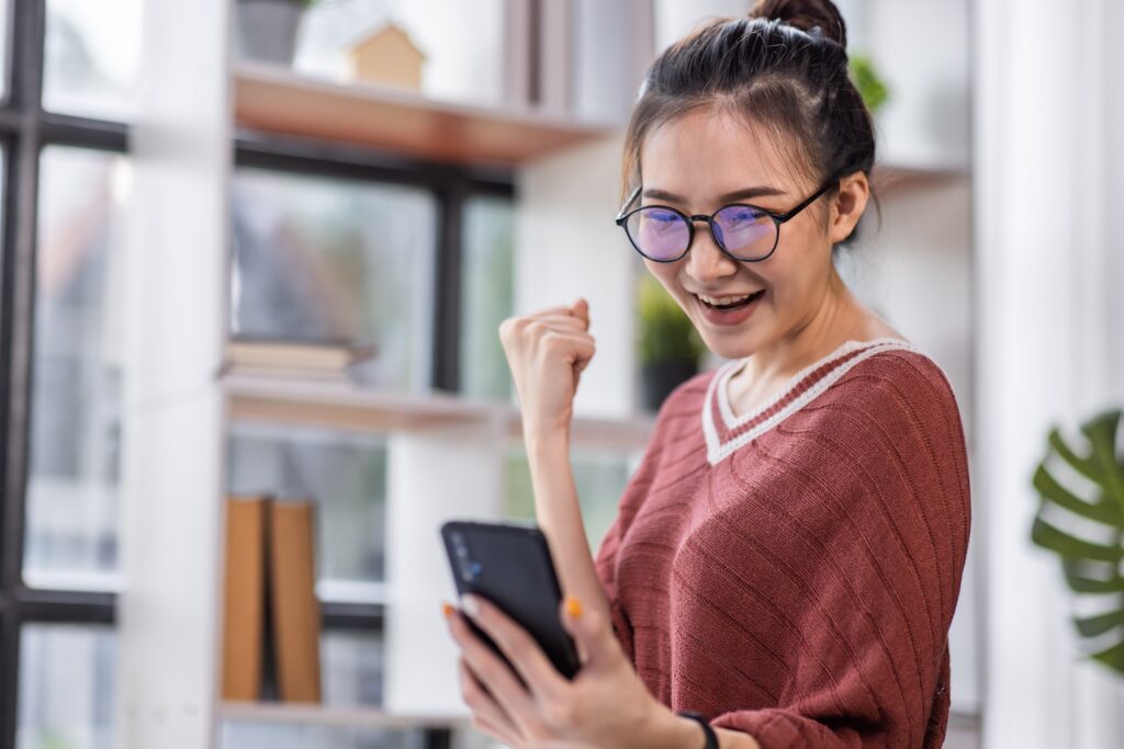 Jeune femme enthousiaste célébrant après avoir complété un sondage LEO sur son smartphone à la maison.