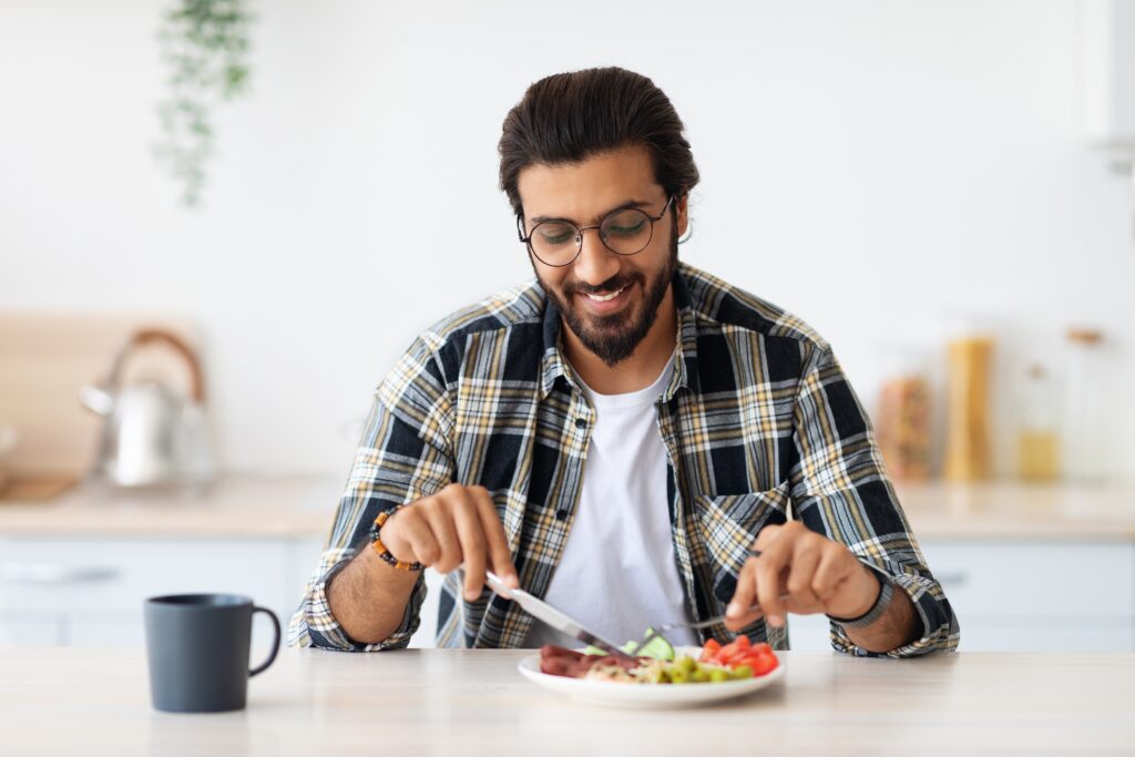 Smiling young man enjoying breakfast at home, starting his day in a relaxed atmosphere while engaging with the LEO platform as part of his daily routine.