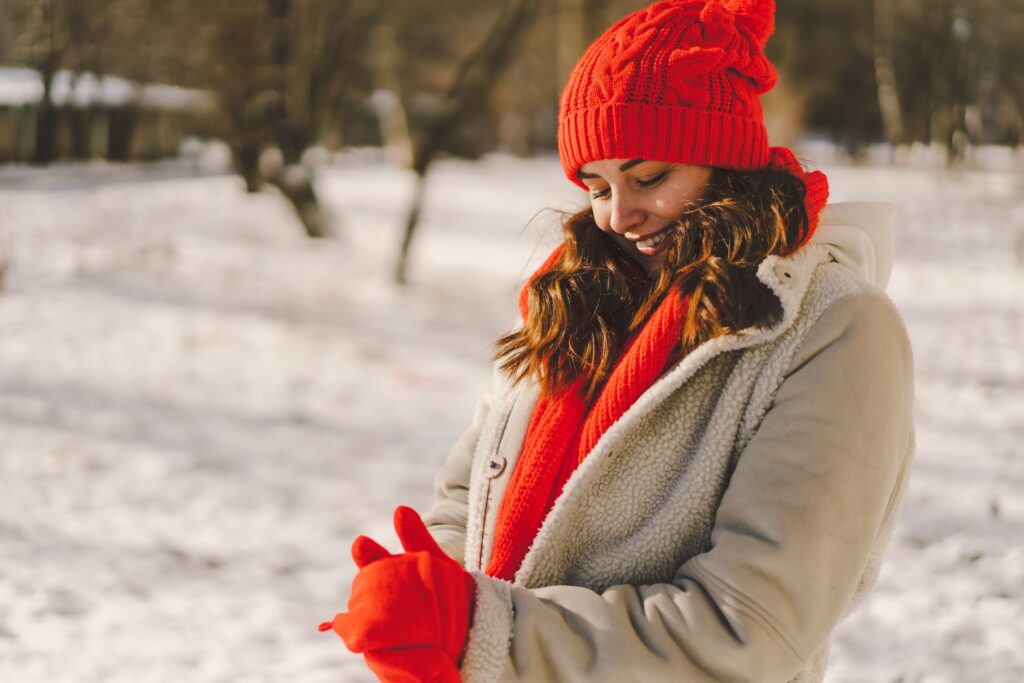 Jeune femme heureuse vêtue pour l’hiver à l’extérieur, souriante et profitant d’une belle journée enneigée.