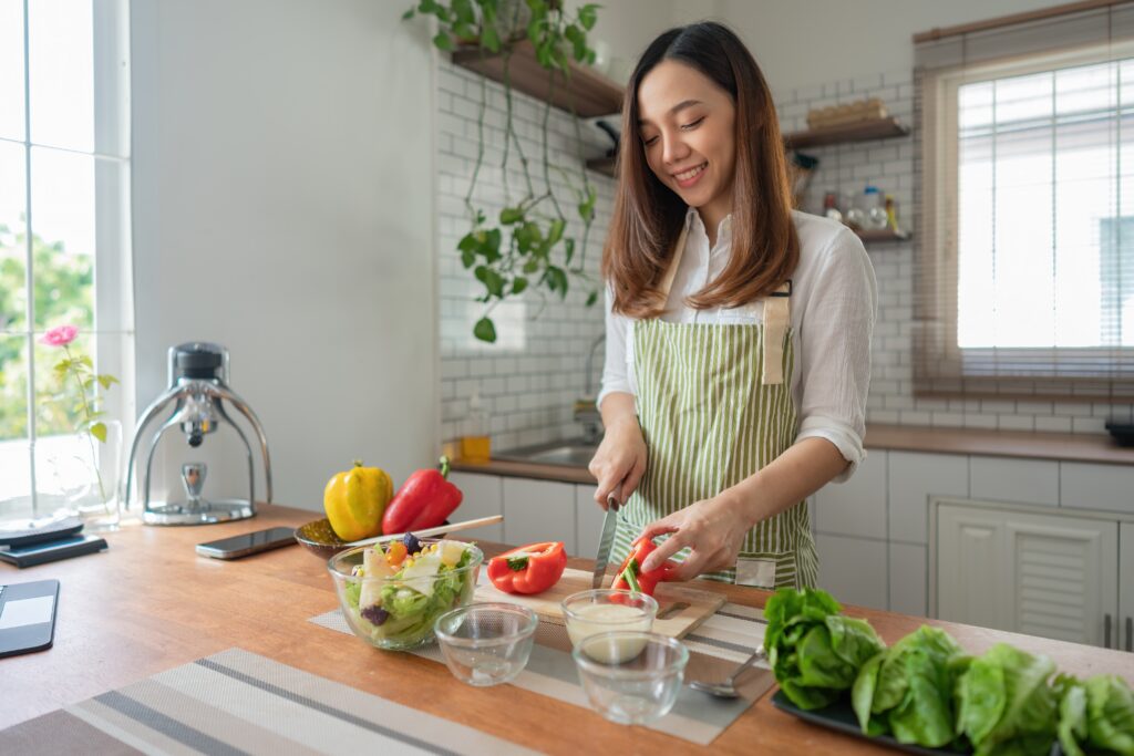 Smiling young woman preparing a healthy meal in her kitchen, enjoying a balanced routine while engaging with the LEO platform as part of her everyday lifestyle.