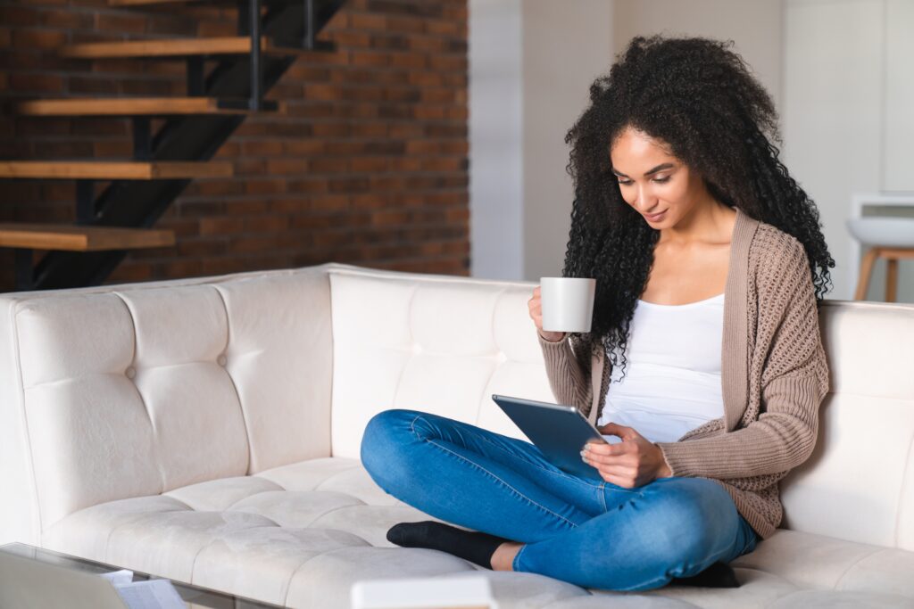 Young woman relaxing on a sofa at home with a cup of coffee, using the LEO platform on a tablet for a calm and convenient digital experience.