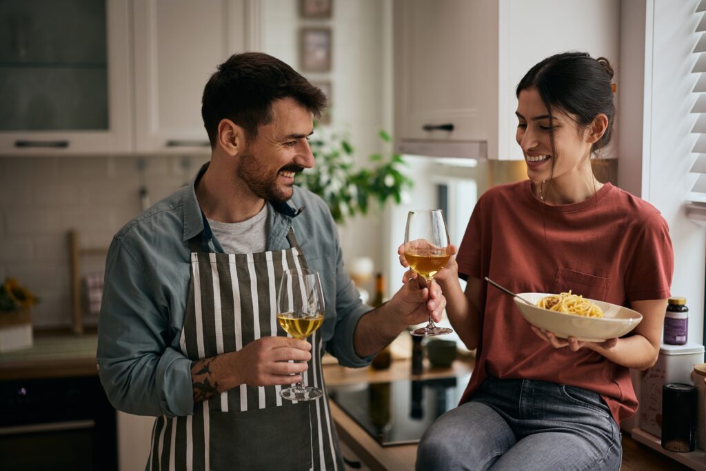 Happy couple cooking together in their kitchen, sharing a toast and enjoying the moment while incorporating the LEO platform into their everyday lifestyle