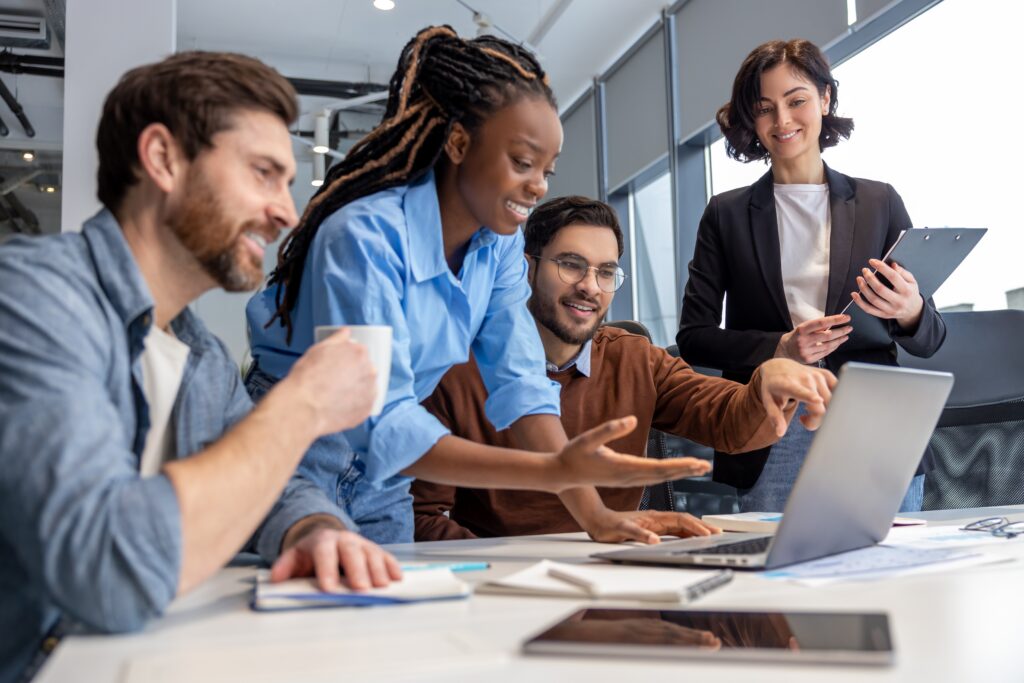 Team of diverse business professionals collaborating in a modern office, smiling and pointing at a laptop while interacting with the LEO platform and its specialized research panels for advanced data insights and audience engagement.