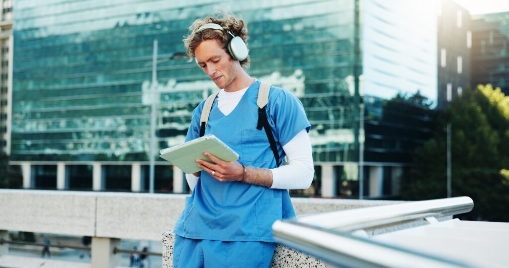 Healthcare professional in blue scrubs standing outdoors in an urban setting, wearing headphones and using a digital tablet while accessing the LEO platform and its specialized research panels.