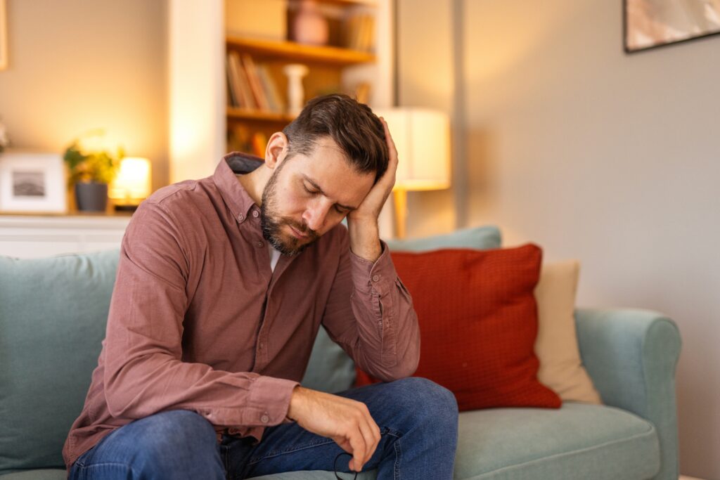Homme assis sur un canapé à la maison avec une expression préoccupée, illustrant le stress et l’anxiété financière abordés dans une étude Léger.
