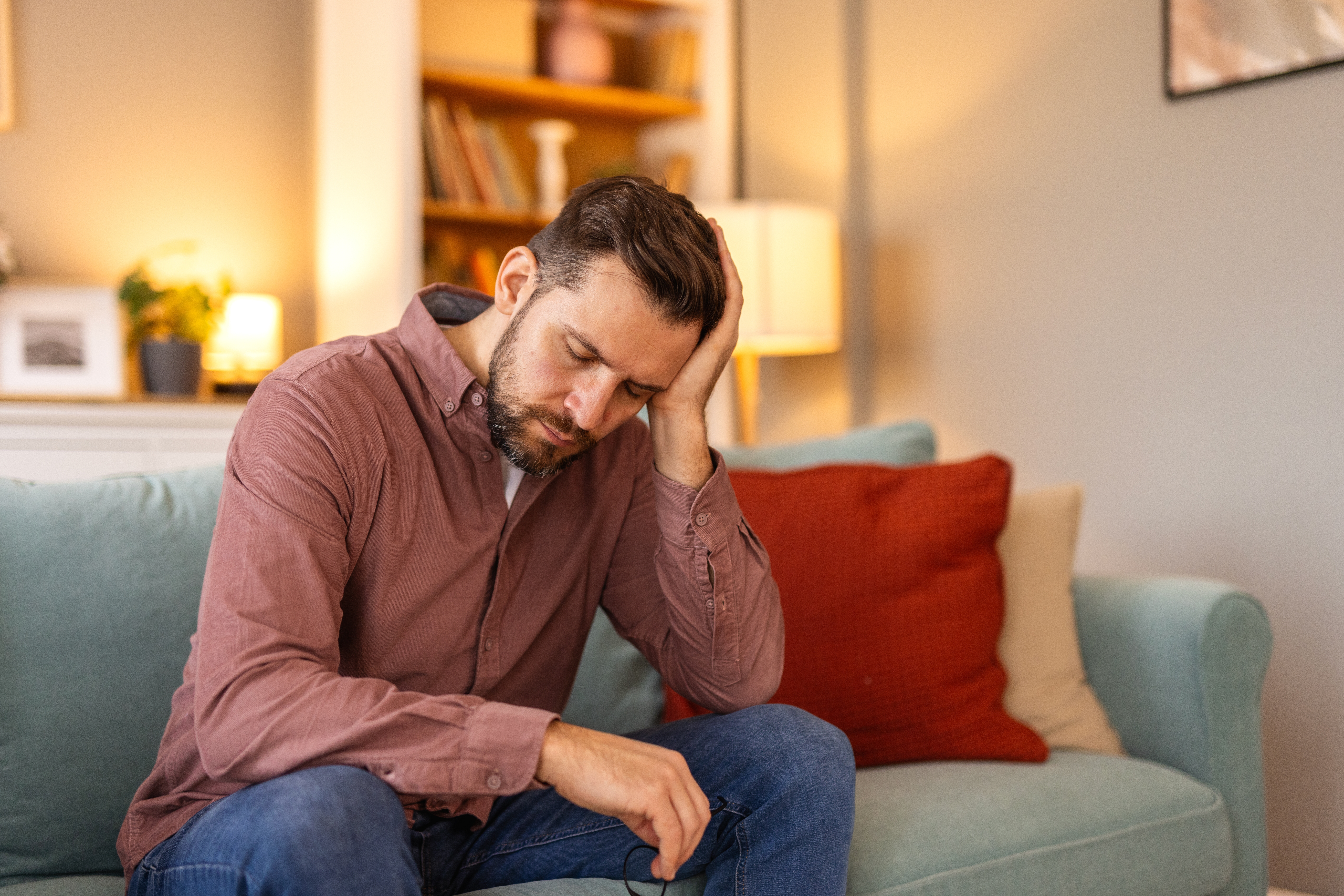 Man sitting on a couch at home with a concerned expression, illustrating stress and financial anxiety discussed in a Leger study.