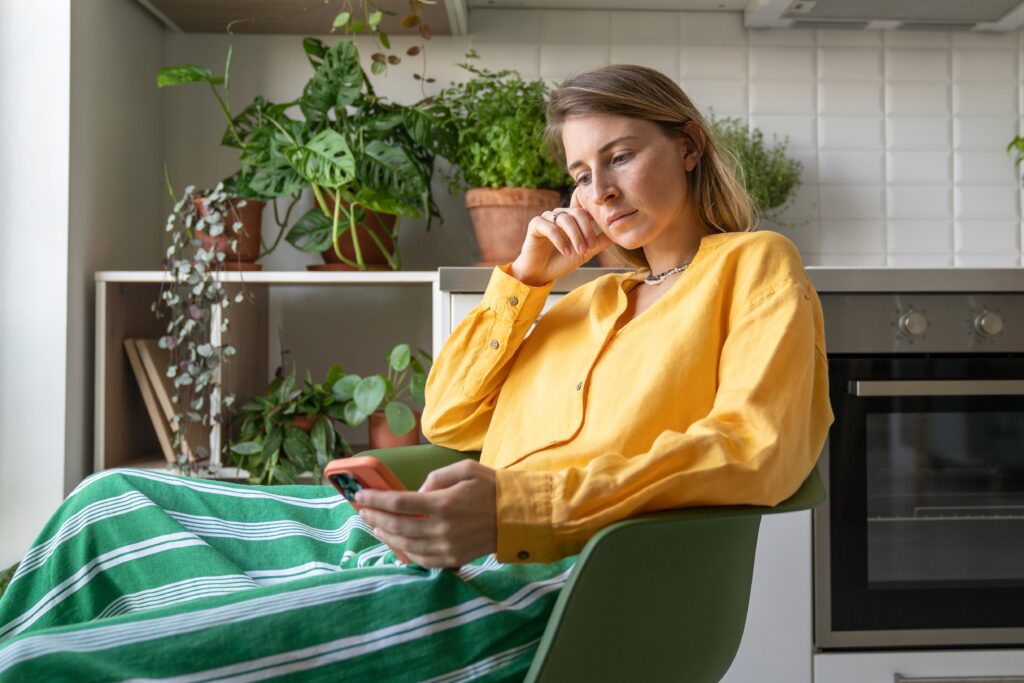 Woman sitting in a modern kitchen, reading a Leger study on her smartphone from the comfort of her home.