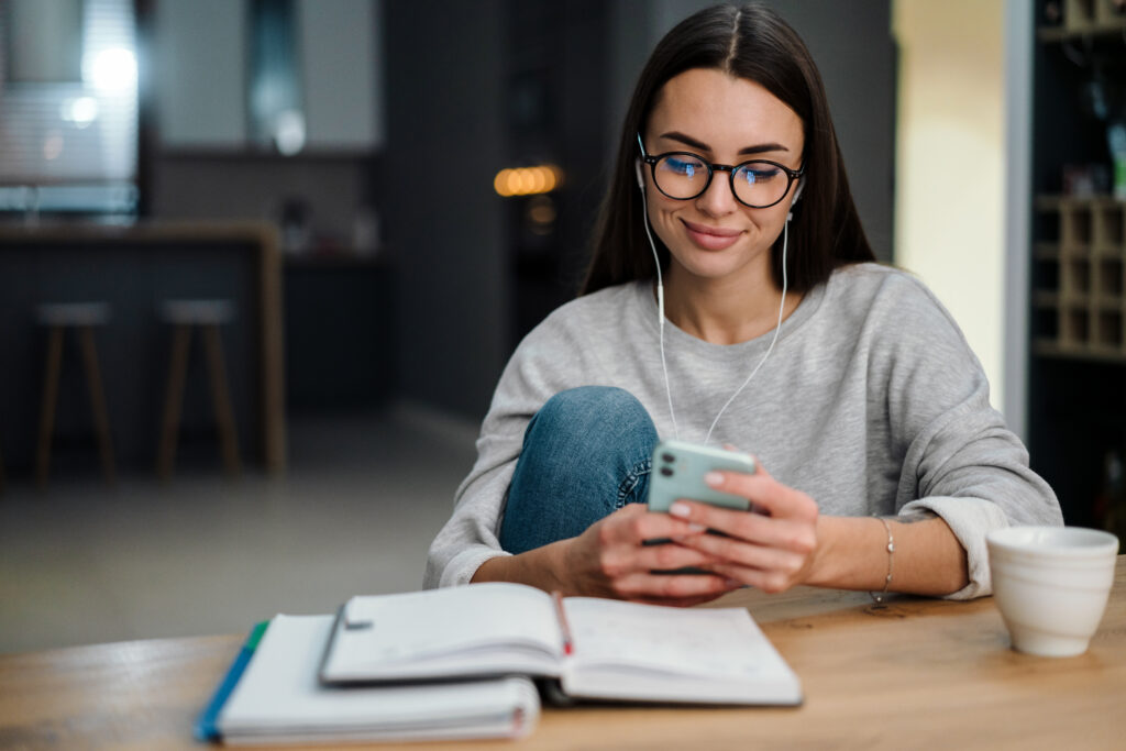 Woman wearing glasses and earphones using her smartphone at home while participating in a LEO contest.