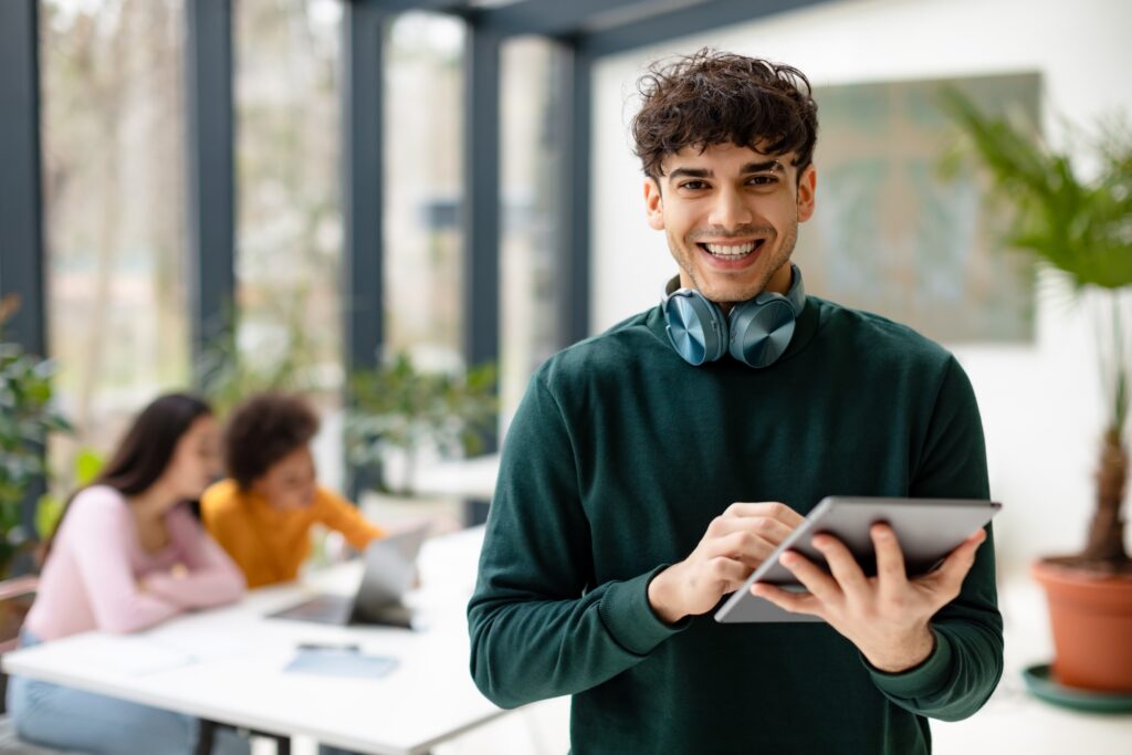 Smiling young man holding a tablet in a modern workspace while participating in a LEO contest online.