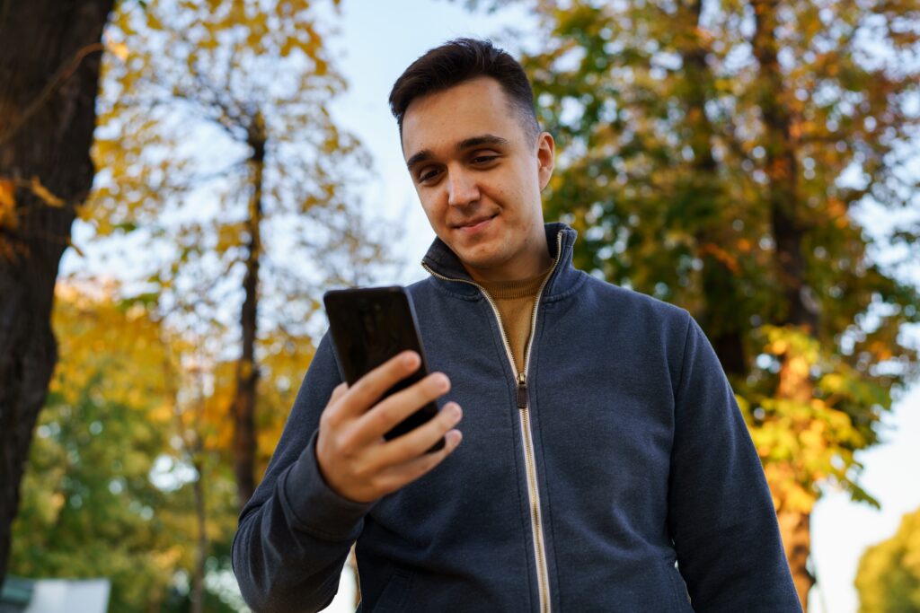 Jeune homme à l’extérieur dans un parc utilisant son smartphone tout en participant à un concours LEO.