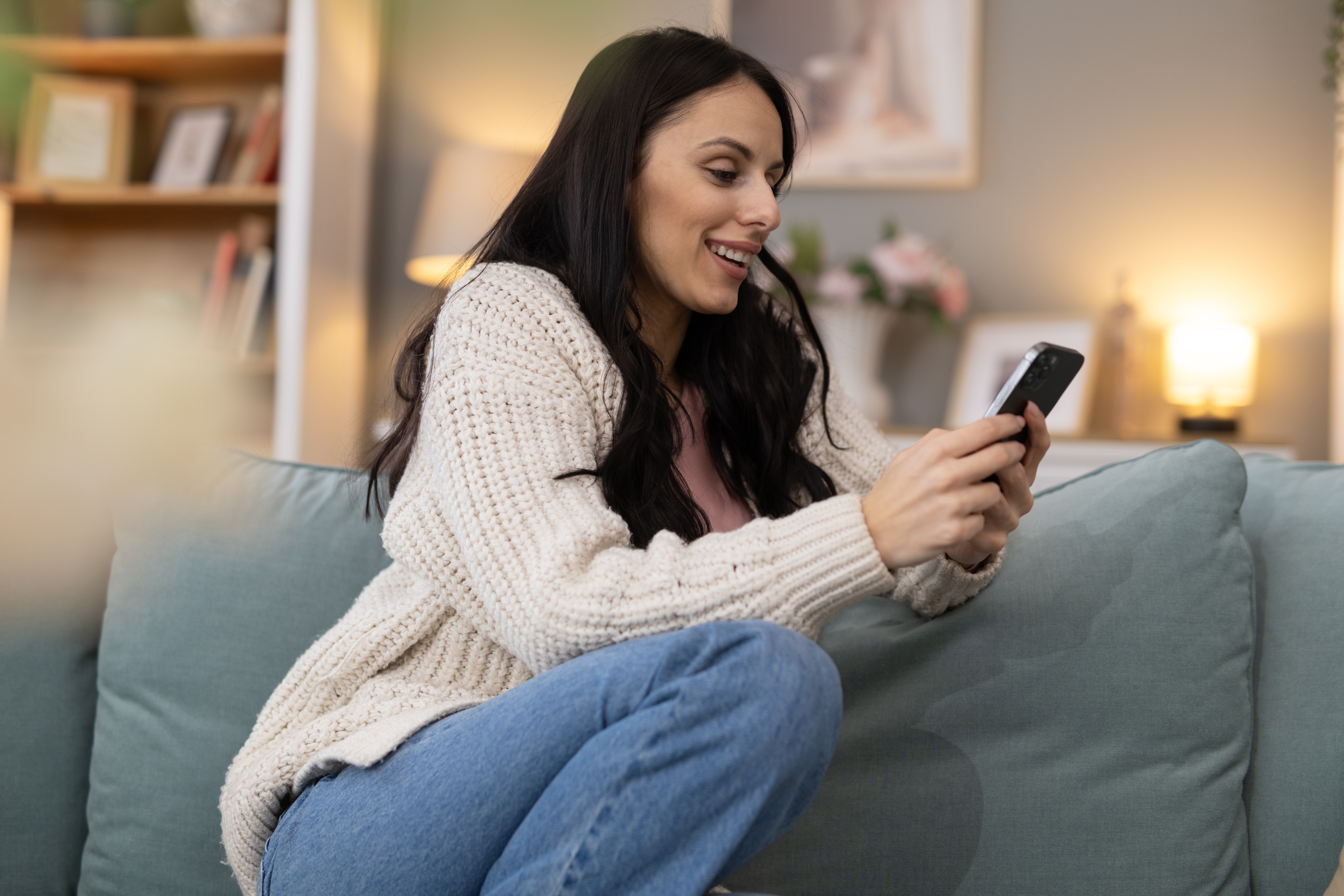 Smiling woman relaxing on a couch at home, using her smartphone while participating in a LEO contest.